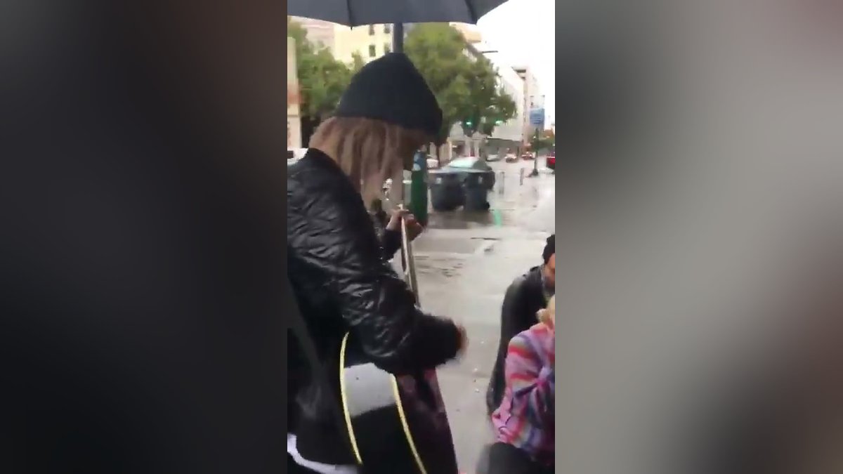 Jovem canta louvor com violão para pessoas em situação de rua na chuva
